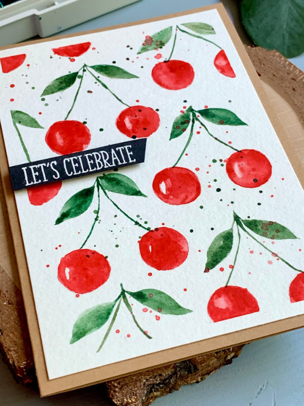 Handmade greeting card with a watercolour cherry background painted with watercolours and a greeting that says Let's Celebrate.