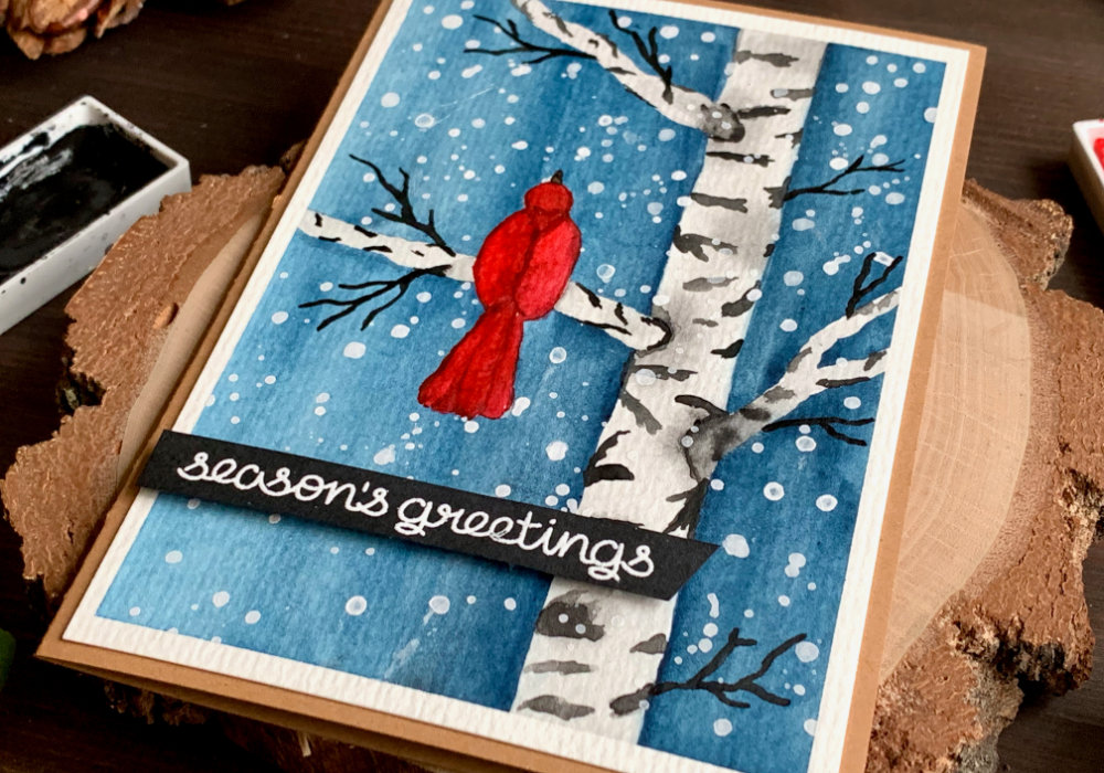 Handmade Christmas card with watercolour snowy winter scene with a birch tree and a red bird sitting on a brunch. The greeting saying 