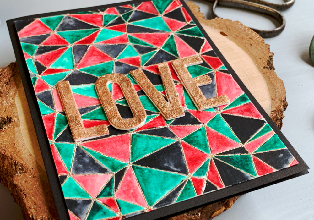 DIY Valentine's day card with stamped and heat embossed background with abstract pattern painted, in three colours - green, red and black and a greeting saying Love, die cut and embellished with gilding flakes in the colour of copper.