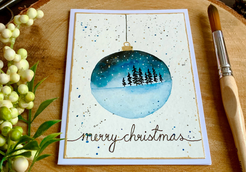 Handmade Christmas card with an ornament decoration with watercolour landscape.