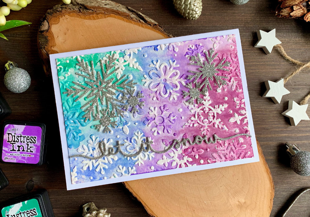 Three DIY Christmas card created with shimmery background created with embossing folders with snowflakes and watercolour products - Nuvo Shimmer Powders, regular watercolours and Distress inks. On top of the cards are glued in snowflakes and greeting die-cut out of a glitter gold and silver card stock.