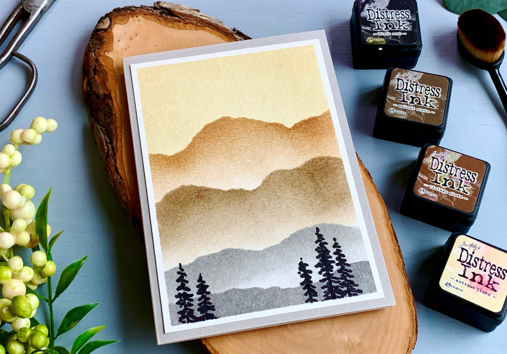 Background for handmade cards made using Distress ink colour combination using the Kit #3 with inks Antique Linen, Vintage Photo, Walnut Stain using a stencil to create a landscape with mountains.