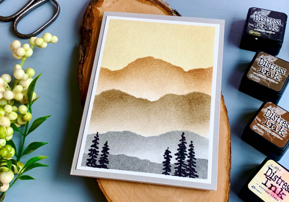 Background for handmade cards made using Distress ink colour combination using the Kit #3 with inks Antique Linen, Vintage Photo, Walnut Stain using a stencil to create a landscape with mountains.