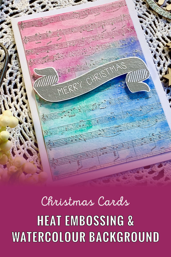 Handmade Christmas card with a stamped, heat embossed music notes and watercoloured background using blue and pink colours.